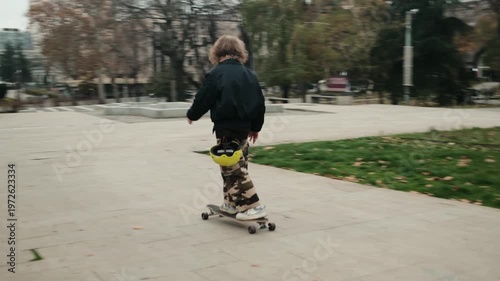 Young man riding longboard along pathway in park surrounded by autumn trees. Urban lifestyle concept with active movement and outdoor freedom. 4k horizontal footage