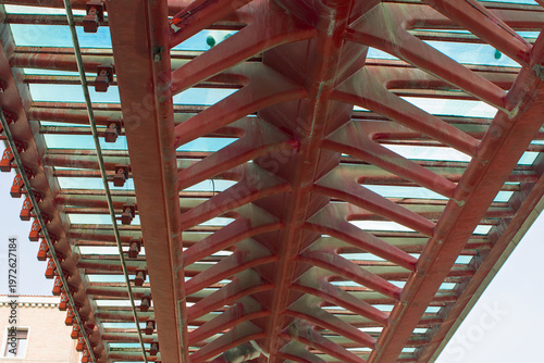 This vibrant red steel architecture features an intricate skeletal design under glass panels. Massive structural beams crisscross through the sky. Ponte della Costituzione, Venice, Italy.