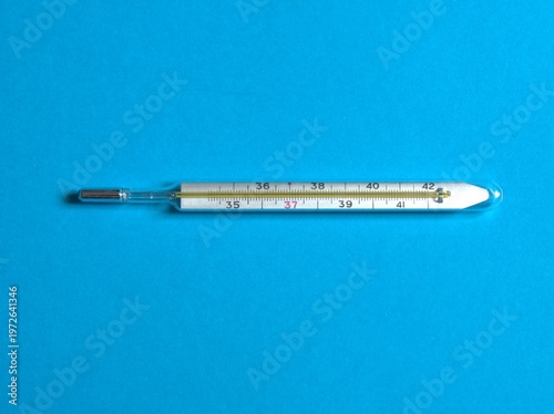 Close-up of a classic glass mercury thermometer placed on a clean blue background. The image represents healthcare, body temperature measurement, fever monitoring, and medical diagnostics.  