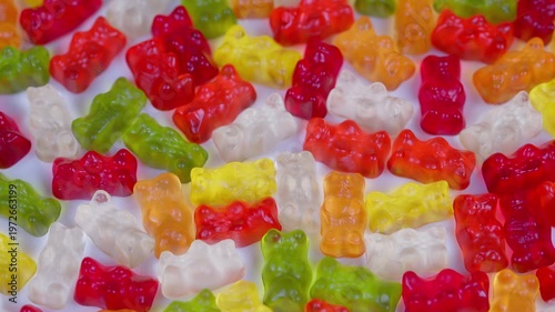 Bright gummy bears showcased vividly. Multicolored translucent candies arranged attractively. Lively and glossy gummy candies in various hues stacked on plain white background
