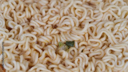 Curly beige noodles with seasoning. Detailed photograph of dry curly noodles. Closeup shot of uncooked curly instant noodles with green flakes and minimalist lighting