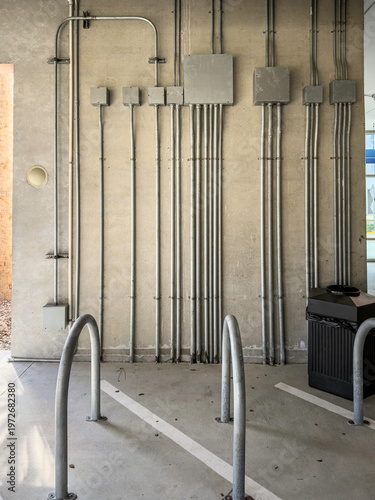 Junction boxes arranged on a wall by U-shaped bollards (impact barriers) along the ground floor of a parking garage by a hospital, for motifs of electrical distribution and safety