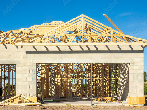 Afternoon shadows of roof trusses crisscross a wall and studs along the interior of a garage of a single-family house under construction in a suburban residential development in southwest Florida