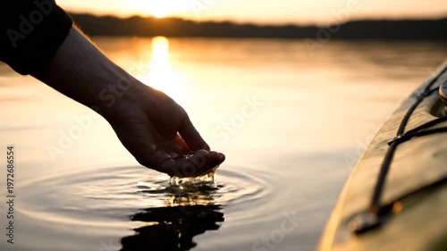 Hand touching calm lake water at sunset next to kayak