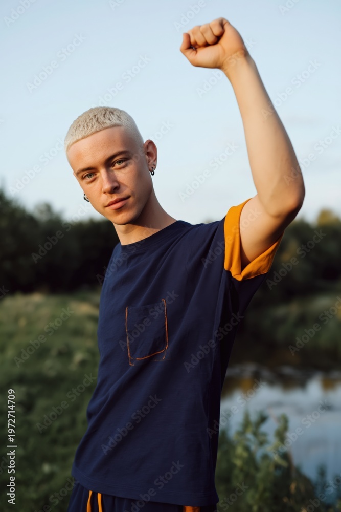 Obraz premium Young man raising fist near riverbank in outdoor park on warm evening