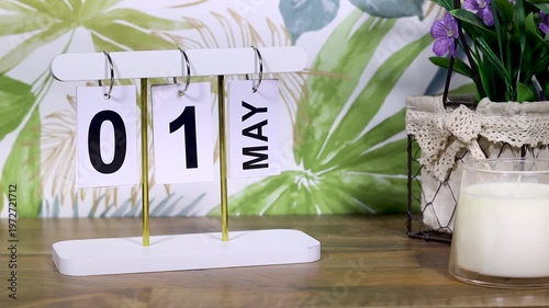 may 1st calendar with candle and flowers near tropical wall on desktop