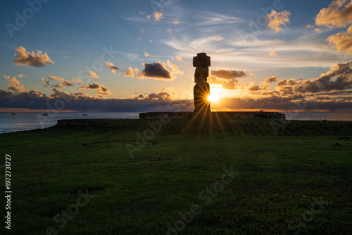 Majestic silhouette of mysterious moai statue on easter island rapa nui during peaceful sunset over ocean with radiant sunburst shining behind ancient stone monument
