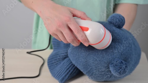 A woman revives the look of her knitted garments with a lint remover.
