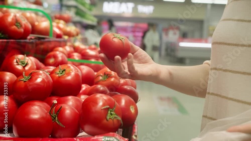 Woman choosing red tomatoes in supermarket produce section.