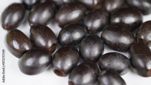 Detailed macro photography showcasing shiny cured black olives with textured skin. Studio closeup image emphasizing glossy appearance and textured surface of cured black olives