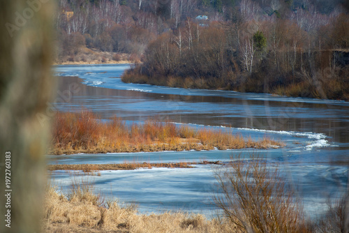 River in Transition: Ice and Water Under Bare Trees