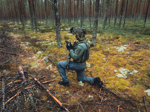 Принти на полотні Military drone pilot in camouflage gear kneeling in a pine forest holding a remo