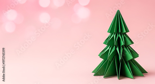 Minimalist green paper folded Christmas tree on pastel pink background. Modern handmade holiday decor and craft art.