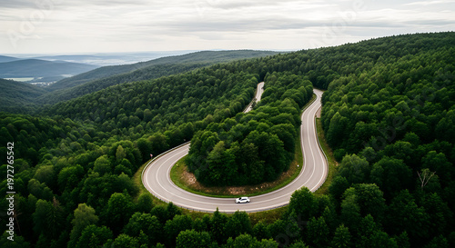 Aerial view of winding forest road with white car in summer. Serpentine asphalt highway through lush green mountains.