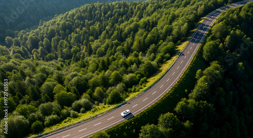 Aerial view of straight asphalt road on mountain ridge at sunset. Highway through green forest hills under warm light.
