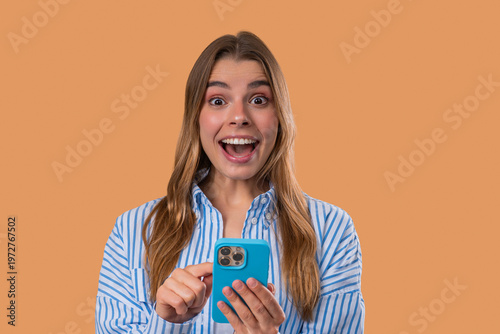 Shocked woman with smartphone on beige studio with open mouth. Amazed lady, app