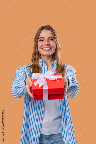 Happy Blonde Woman Gift Box On Beige Background. Young Girl Smiling, Gives You