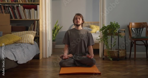 A young man practices meditation in a warm, inviting bedroom that radiates tranquility and focus