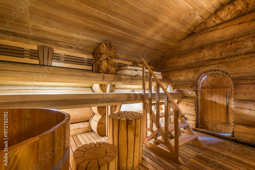 Tableau sur toile The interior of a wooden sauna shows benches on two levels, a wooden staircase, and a round tub