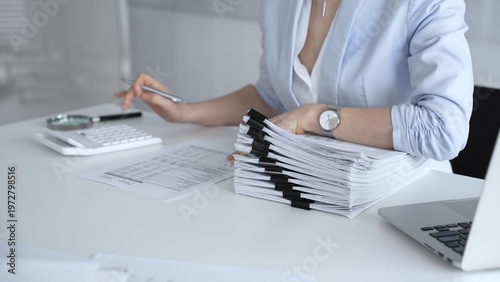 Photos Businesswoman managing heavy workload, organizing documents, accounting for taxes, planning financial reports, processing paperwork, and working with pile of files in modern office