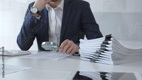 Bild auf Leinwand Professional accountant or auditor carefully examining financial documents and corporate reports with a magnifying glass, diligently researching tax obligations and legal compliance