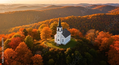 A white church atop a hill surrounded by autumn foliage; sunlit mountains in the background