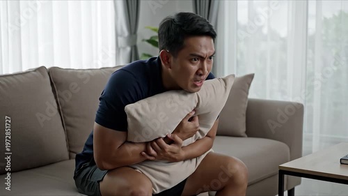 Man sitting on couch with pillow, stressed and anxious expression, watching something intently