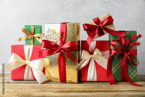 Many gift boxes with decor on wooden table near grey wall, closeup. Merry Christmas and Happy New Year