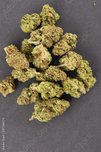 Close-up of dried cannabis buds with green and orange hues arranged on a dark surface.