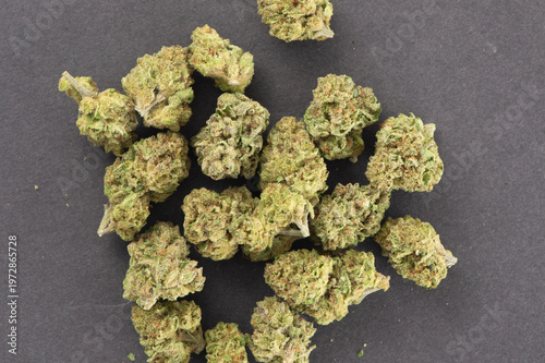 Dried cannabis buds scattered on a dark surface, showing a close-up of the green, textured flower clusters.