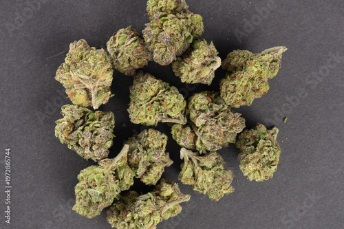 Dried cannabis buds arranged on a dark surface displaying green and orange hues typical of marijuana flowers.