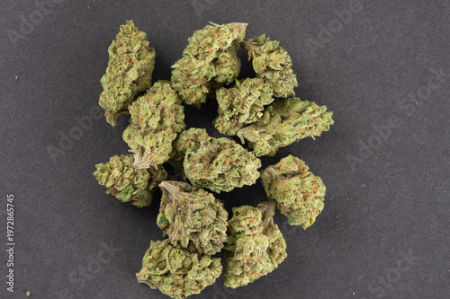 Dried cannabis buds with green and orange hues displayed on a dark surface.