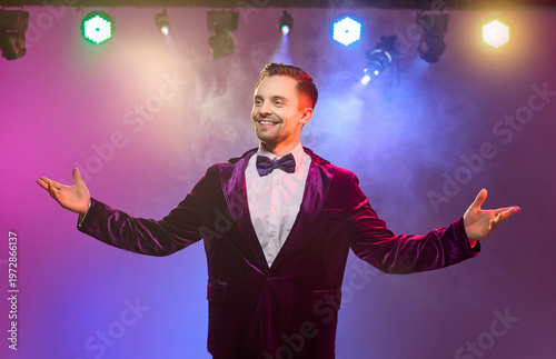 Showman host presenter man smile on stage lights. Cheerful emcee spreads arms in colorful haze, exuding charm and confidence for party promos and event visuals. A true sign of success.