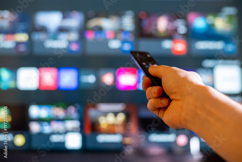 Hand Holding TV Remote Toward Blurred Smart TV Streaming Screen