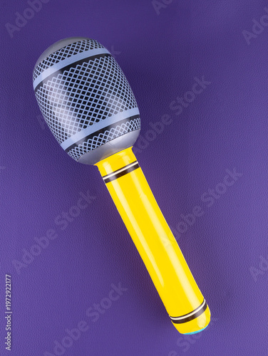 Close-up of a fun  yellow inflatable microphone toy for entertainment on a purple background.