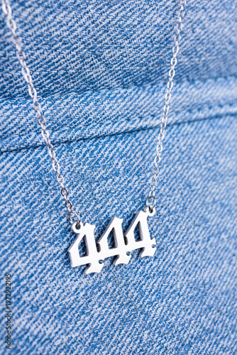 Close-up of a silver  pendant with the number 444 on a chain, set against a  blue background.