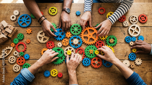 Top down flat lay overhead view of multiple diverse hands collaborating to connect colorful wooden gears and cogs into a complex mechanical system on a desk
