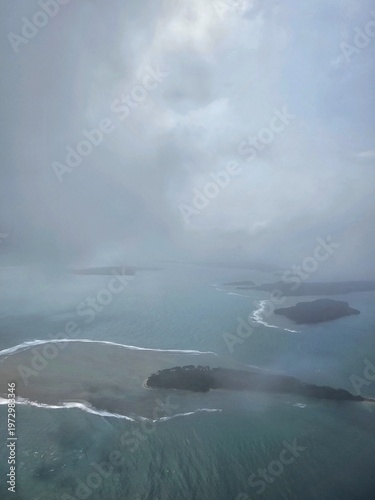 Dramatic overcast aerial shot looking down at dark landmasses and shallow turquoise reefs of the Andaman and Nicobar Islands scattered in the sea.