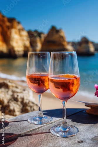 Two glasses of rose wine on a table overlooking a beautiful beach and ocean.