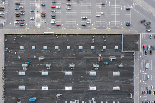 shopping mall shingle roof with ventilation system and skylights. parking lot with parked cars. aerial top view.