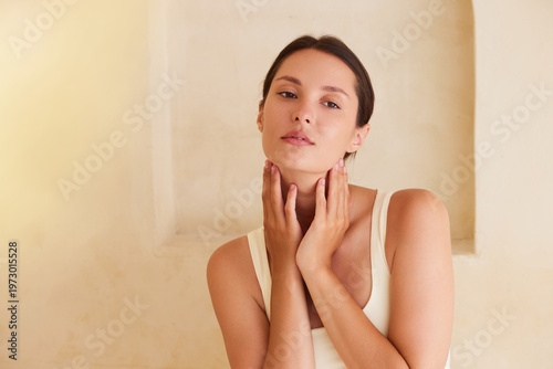 Minimal beauty portrait of a woman touching her neck with clean glowing skin, soft natural light and neutral background. Ideal for skincare, wellness, anti aging and beauty concepts.
