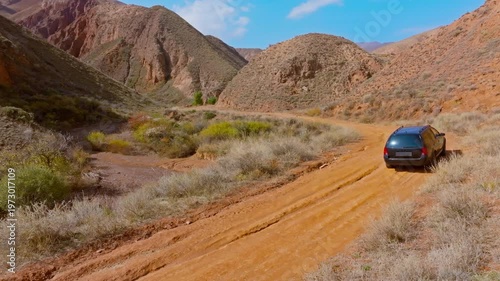 Car drives along dirt road in eroded sandstone mountains of Kyrgyzstan. Static camera view. Scenic landscape captures adventurous spirit in peaceful daytime setting.