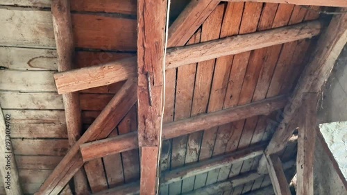 Aged wooden beams and planks arranged in triangular truss pattern, dim lighting highlighting rustic textures, capturing the worn detail of an old attic or barn roof