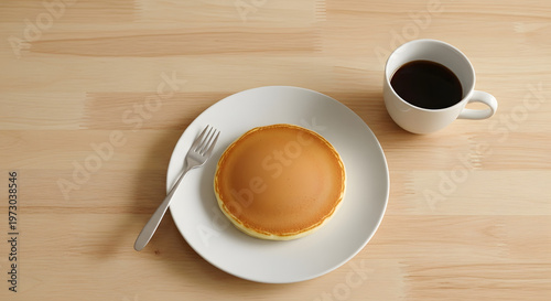 A single golden pancake on a white plate with a fork and a mug of black coffee on a light wooden table, ready for breakfast.