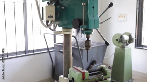 Vertical Drill Press Machine in Industrial Workshop with Metal Shavings and Bench Grinder Background
