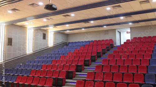 Interior View of Modern Lecture Theater with Empty Red and Blue Seating Tiers and Ceiling Projector.
