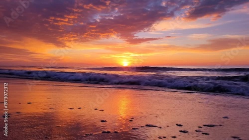 Vibrant sunset with orange and purple clouds over a calm ocean as small waves gently lap onto the sandy beach during the golden hour at dusk in a tropical coastal landscape.