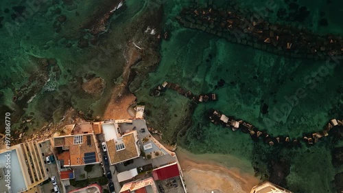 Aerial view of coastal town in Sicily at dawn, showcasing colorful buildings, sandy beach, and rocky shoreline with clear turquoise waters and wooden structures