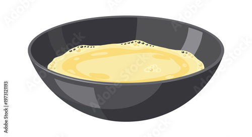 A close-up view of a dark bowl containing a creamy yellow liquid with small bubbles forming on its surface, presented on a clean white background