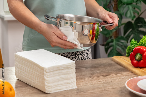 Side view. A housewife uses paper white napkins to wipe a pot. Horizontal photo. Cleanliness and kitchen cleaning. Lifestyle.